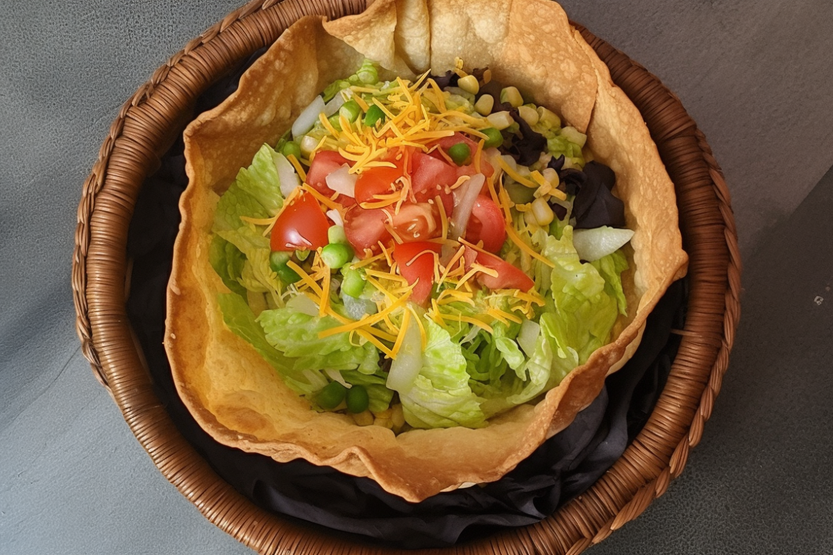 Freshly baked crispy tortilla bowl filled with lettuce and tomatoes.